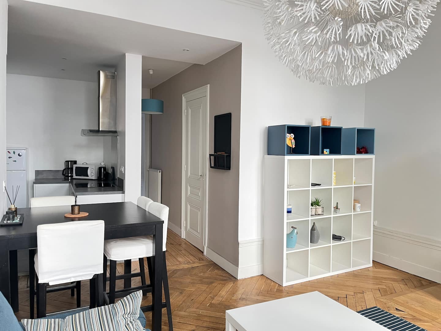 Coin repas avec table et chaises blanches, étagère à casiers et cuisine ouverte