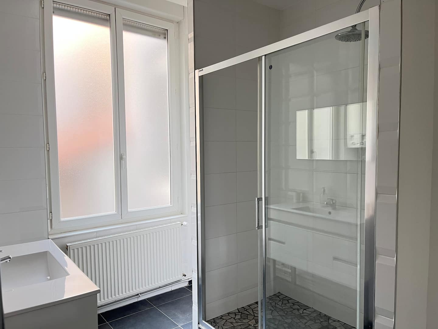 Salle d’eau avec cabine de douche vitrée, vasque et fenêtre